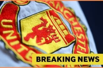 Close-up image of Manchester United logo with yellow breaking news banner