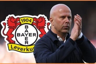 Arne Slot claps his hands with Bayer Leverkusen club crest behind him.