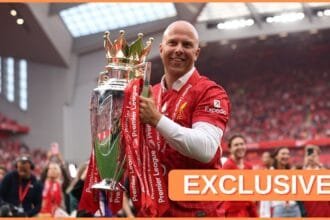 Arne Slot holds the Premier League trophy on the pitch at Anfield.