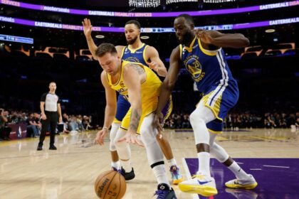 Luka Doncic #77 of the Los Angeles Lakers reaches for the ball while being protected by Draymond Green #23 and Stephen Curry #30 of the Golden State Warriors