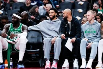 Boston Celtics #0 Jayson Tatum and #9 Derrick White watch from the bench as their team plays against the Toronto Raptors during the first half of a preseason basketball game.