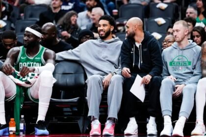 Boston Celtics #0 Jayson Tatum and #9 Derrick White watch from the bench as their team plays against the Toronto Raptors during the first half of a preseason basketball game.