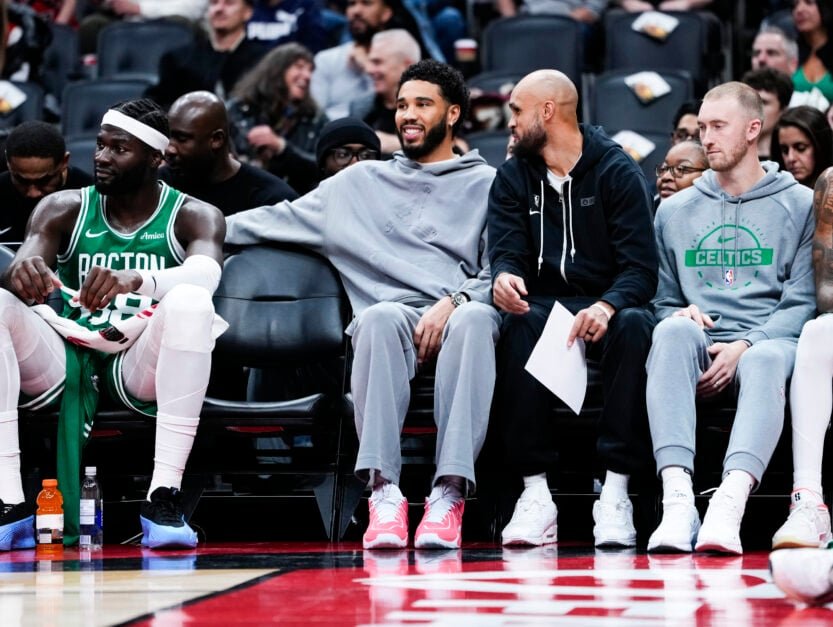 Boston Celtics #0 Jayson Tatum and #9 Derrick White watch from the bench as their team plays against the Toronto Raptors during the first half of a preseason basketball game.